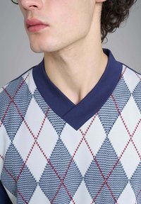 Maglione da uomo in maglia con collo a V blu navy, motivi a rombi in blu e rosso, e un tessuto leggero e strutturato.