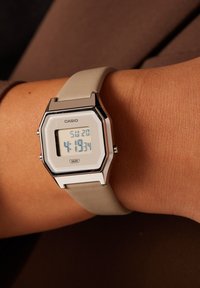 Montre numérique Casio avec un boîtier octagonal en argent, un bracelet en silicone gris clair et un affichage numérique montrant l'heure et la date.