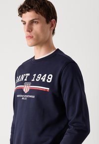 Marine sweatshirt met een ronde hals, witte letters, een schildlogo en rode en witte strepenaccenten. Gemaakt van een katoenmix met een gladde textuur.