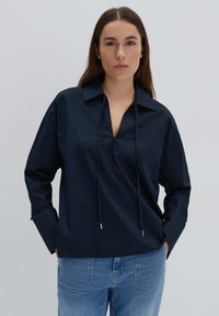 Maglietta blu navy con scollo a V e dettaglio con cordino, dotata di maniche lunghe e vestibilità rilassata, realizzata in tessuto leggero.