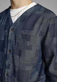 Mörkblå mönstrad kofta med en strukturerad tyg, som har geometriska mönster, knappar och en ficka på vänster sida.