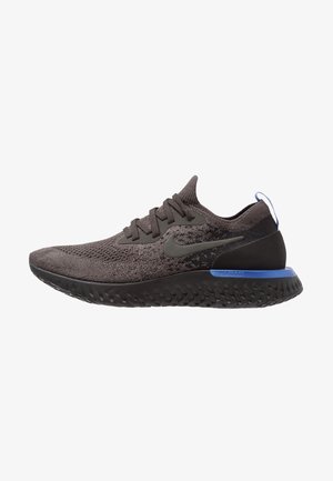 Zapatilla de running Nike gris oscuro con parte superior de punto, suela negra, acento azul en el talón y cordones, mostrada en perfil lateral sobre fondo blanco.