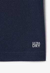 Granatowy materiał odprowadzający wilgoć z teksturowaną powierzchnią, z białym logo "ULTRA DRY" blisko dolnego brzegu. Starannie wykończone szwy.