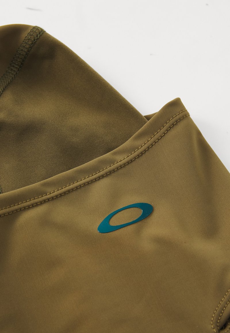 Olivgrüner Sportstoff mit glatter Textur, ausgestattet mit flachen Nähten und einem blauen Logo-Akzent. Entworfen für Leistung und Komfort.