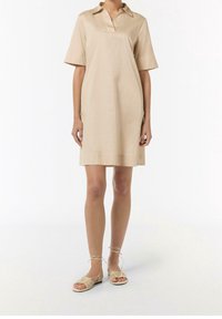 Vestido corto beige de manga corta con cuello, textura suave, largo hasta la rodilla, combinado con sandalias nude de tiras. Diseño simple sin patrones.