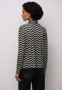 Czarna i kremowa kurtka w wzór zygzak z wyraźnym kołnierzem i długimi rękawami. Materiał wydaje się gładki, z dopasowanym krojem.