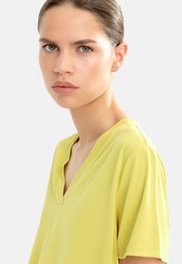 Koszula z dekoltem w serek i krótkim rękawem w jasnym żółtym kolorze, wykonana z miękkiego materiału o gładkiej fakturze, charakteryzująca się luźnym krojem i minimalną ilością szwów.