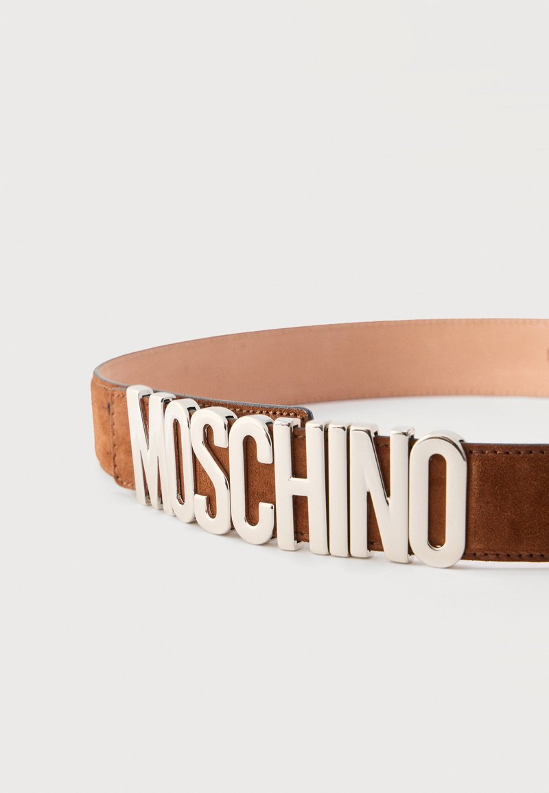Brown suede belt with large silver metal letters spelling "MOSCHINO" as the buckle on a plain white background.