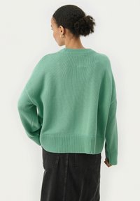 Pull surdimensionné en tricot côtelé de couleur vert clair, avec un col rond et des épaules tombantes, associé à une jupe noire à la texture lisse.