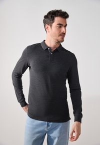 Tmavě šedá polokošile s dlouhým rukávem, dvoubotkovou légou a jemnou texturou, v kombinaci se světle modrými džíny.