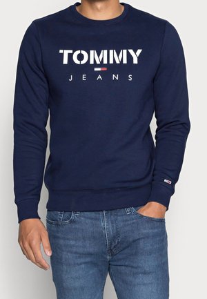Granatowy sweter wykonany z mieszanki bawełny, z wyraźnym logo "TOMMY JEANS" w kolorze białym, okrągłym dekoltem oraz ribbowymi mankietami i detalem wzdłuż dołu.