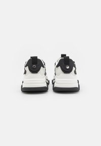 Black and white athletic sneakers with a textured mesh upper, thick white midsole, and black outsole. Featuring pull tabs at the heel.