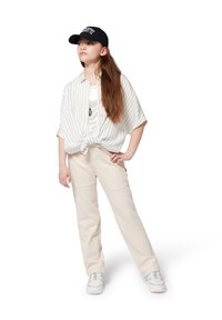 Chemise blanche  à rayures, à manches courtes, nouée à la taille, associée à un pantalon beige et des baskets blanches, surmontée d'une casquette noire avec "NAVY".