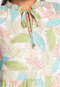 Kevyt pusero, jossa on kerätty pääntie ja nauha. Kukallinen lehtikuvio pastelliväreissä sinistä, vaaleanpunaista ja vihreää valkoisella taustalla.