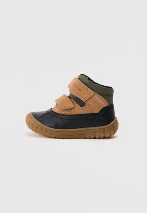 Botte imperméable pour enfant jusqu'à la cheville avec lanières en daim marron, bout noir, col en tissu vert et semelle en caoutchouc marron texturée, orientée vers la gauche.