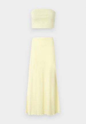 Set din două piese format dintr-un top fără bretele și o fustă lungă, fluidă. Confecționat dintr-un material ușor, de culoare galbenă deschisă, cu o textură netedă și fără modele.