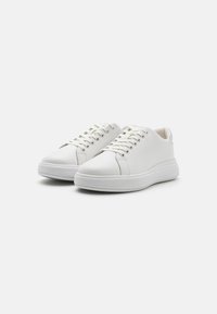 White leather sneakers with a smooth texture, round toe, thick white rubber sole, and silver accent at the heel. Features lace-up closure.