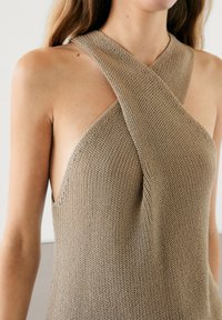 Knit halter top in beige, featuring a crisscross neckline, open sides, and a textured fabric. Simple, form-fitting design.