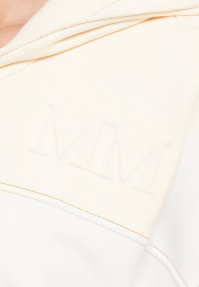 Cream hoodie featuring embossed "MM" logo on the chest, soft texture, and contrasting stitching along the seams.