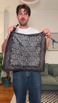 Fekete bandana fehér paisley mintával, keretes dizájnnal és sima textúrával, egy személy kezében, laza környezetben.