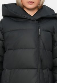 Sort pufferjakke med hætte, lynlåslukning og kviltet design med synlig polstring. Glat, mat tekstur med minimale accenter.