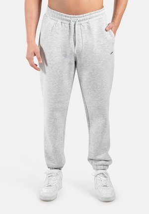 Graue Jogginghose mit elastischem Bund, Seitentaschen und elastischen Bündchen, aus einem weichen Baumwollmix gefertigt. Getragen mit weißen Sneakers.