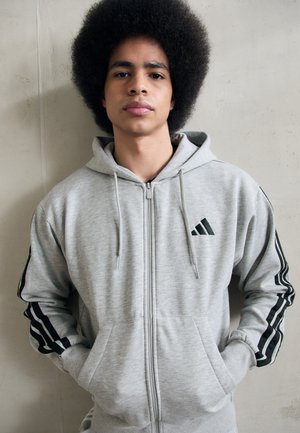 Grey zip-up hoodie with black striped accents on sleeves and logo on chest; front pockets; soft, textured fabric.