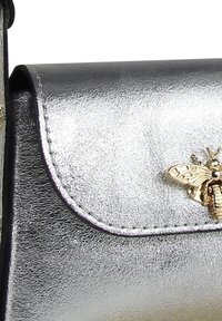 Sac à main en argent métallique avec un rabat courbé, orné d'un accent abeille doré et de coutures détaillées le long des bords.
