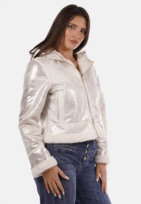 Giacca metallica argento lucido con zip frontale, cappuccio e finiture in pelliccia sintetica. Caratterizzata da due tasche frontali e design cropped.