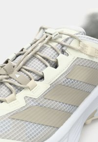 Αθλητικό παπούτσι με γκρι επάνω μέρος από δίχτυ, ανοιχτό μπεζ λεπτομέρειες, δεμένα κορδόνια και τρεις μπεζ ρίγες στο πλάι, με υφή σόλας.