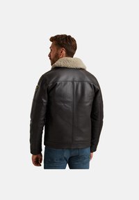 Čierna kožená bunda s ovčím golierom, hladká textúra, horizontálne prešitie na leme a detail loga na ľavom ramene.