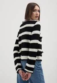 Maglione lavorato a maglia a strisce bianche e nere con una vestibilità corta, bordi sfrangiati e spacchi laterali, abbinato a jeans blu a vita alta.