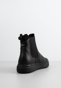 Les bottines Chelsea en cuir noir présentent des panneaux latéraux élastiques, une languette de tirage marquée à l'arrière, et une semelle en caoutchouc texturée.
