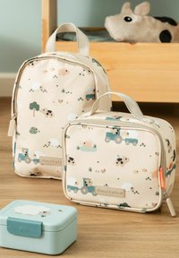 Sac à déjeuner beige pour enfants et sac à dos avec motif d'animaux de la ferme et de tracteur sur un sol en bois, peluche en arrière-plan.