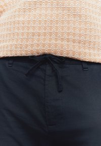 heleoranž tooniga mustriga topp, mida on kombineeritud tumeda mereväe pükstega, millel on nöörist vöökoht ja sile linase tekstuur.