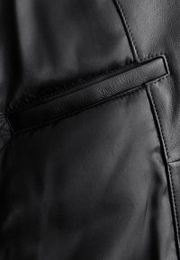 Gros plan sur une poche de veste noire avec un tissu lisse et une bordure en cuir texturé cousue autour de l’ouverture.