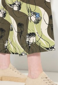 Grön och beige klänning med blomsterdesign och svarta konturer, kombinerad med ljusbeige espadrillos med snören och en vävd sula.