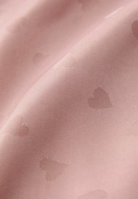 Tissu rose clair présentant une texture lisse avec un motif de cœurs subtile, créant une apparence délicate mais structurée.