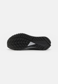 Zwarte sneakersole met een gestructureerde rubberen loopzool voorzien van multidirectionele groeven en een zilveren driehoekaccent bij de hiel.