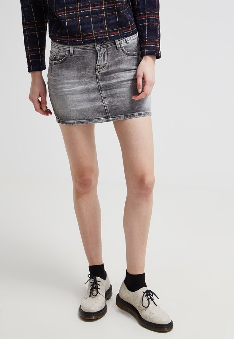 Džínová mini sukně ve světle šedé barvě, s klasickým designem pěti kapes, nošena s černými kotníkovými ponožkami a světle zabarvenými šněrovacími botami.
