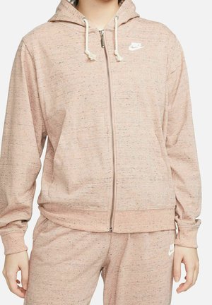 Vaaleanpunainen vetoketjullinen huppari, jossa on teksturoitu kangas, kiristysnauhallinen huppu ja etutaskut. Vasemmassa yläkulmassa valkoinen Nike-logo.