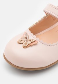 Růžová kožená bota se zvlněnými okraji a lesklým akcentem ve tvaru motýla. Hladký povrch a kulatá špička s béžovou podrážkou.