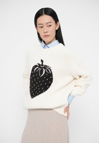 Valkoinen neulepusero, jossa suuri musta mansikkakuosi. Pyöreä pääntie, rento istuvuus ja resorit hihansuissa. Yhdistetty sinisen kauluksellisen paidan kanssa.