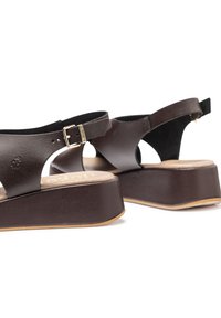 Sandales compensées en cuir brun avec un design découpé, une bride de cheville réglable et une plateforme texturée. Détail en boucle dorée.