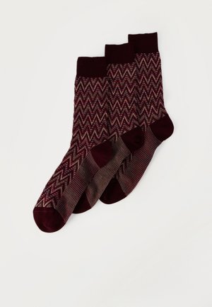 Trois chaussettes bordeaux avec des motifs en zigzag et petits points, présentant talons et orteils en bordeaux plus foncé uni, disposées en chevauchement sur un fond blanc.