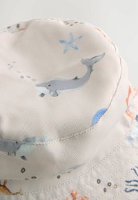 Jasny kapelusz typu bucket, wykonany z materiału, z morskimi wzorami przedstawiającymi delfiny, rozgwiazdy i koralowce w delikatnych odcieniach niebieskiego i pomarańczowego.