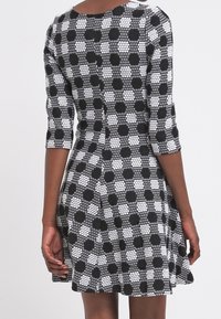 Czarna i biała sukienka w wzory z rękawami do trzech czwartych, dopasowanym gorsetem, rozkloszowaną spódnicą i okrągłym dekoltem. Detale w postaci kropek i heksagonalnej tekstury.