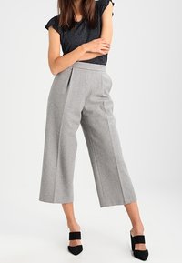 Šedé elegantní culoty z měkké látky, s sklady a vysokým pasem. Spárovány s texturovaným černým topem a černými podpatky.