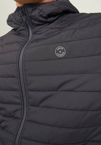 Padded jacket in dark navy, featuring a zip front, hood, and horizontal stitched design. Logo patch on the left chest. Smooth fabric texture.