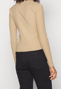 Beige räfflad långärmad topp med en figurnära design, som har en hög halsringning och en slät textur, matchad med svarta högmidjade jeans.